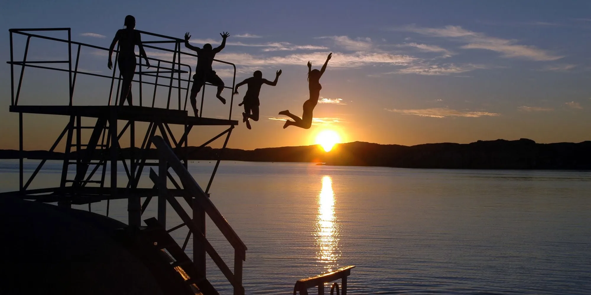 Vier Jugendliche springen vom Sprungturm direkt in den Sonnenuntergang