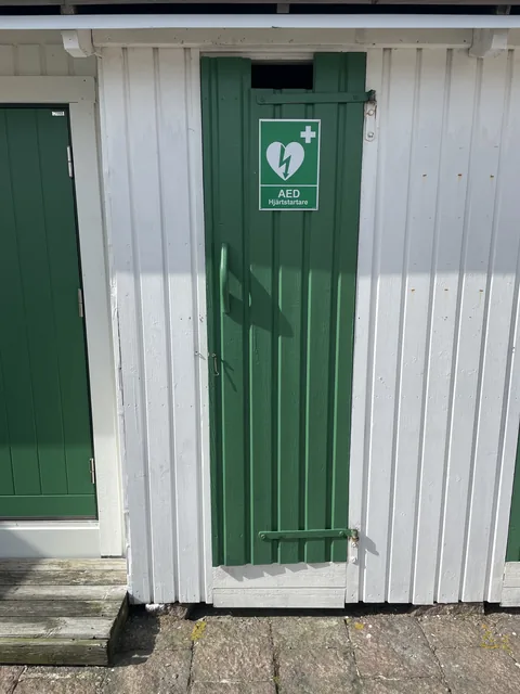 The bathing hut nearest the kiosk, with the sign AED Defibrillator on the green door