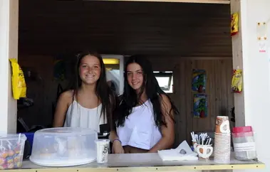 Two summer staff at the kiosk hatch with sweets, coffee cups and the ice cream freezer